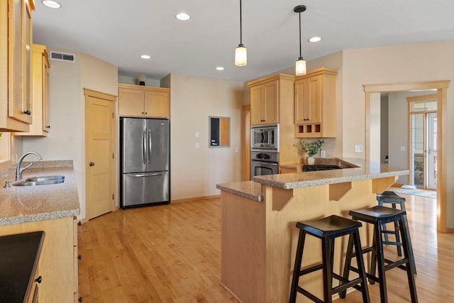 kitchen with light brown cabinets, a sink, stainless steel appliances, a peninsula, and light wood finished floors