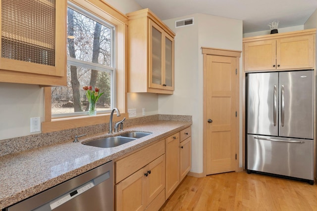 kitchen with light brown cabinets, a sink, light wood-style floors, appliances with stainless steel finishes, and light stone countertops