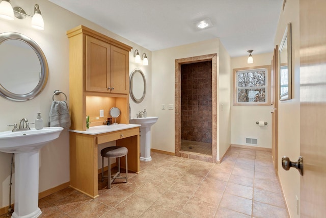 bathroom featuring visible vents, a tile shower, tile patterned flooring, baseboards, and two sinks