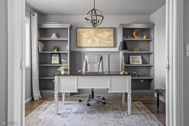 office area featuring a chandelier, built in shelves, baseboards, and wood finished floors