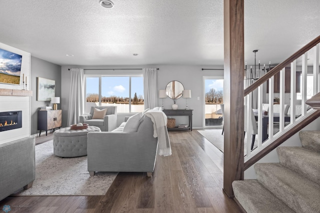 living room featuring stairs, an inviting chandelier, wood finished floors, a glass covered fireplace, and a textured ceiling