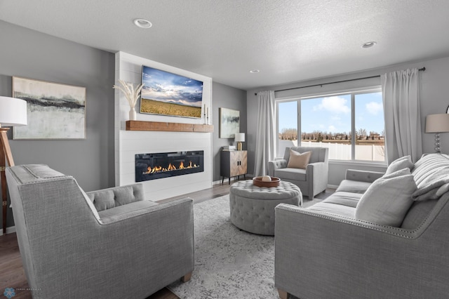 living room with a textured ceiling, wood finished floors, a glass covered fireplace, recessed lighting, and baseboards