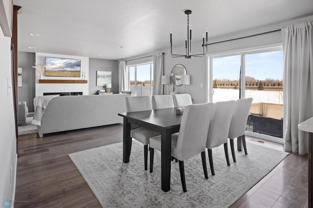 dining space featuring wood finished floors, visible vents, a fireplace, a textured ceiling, and a chandelier