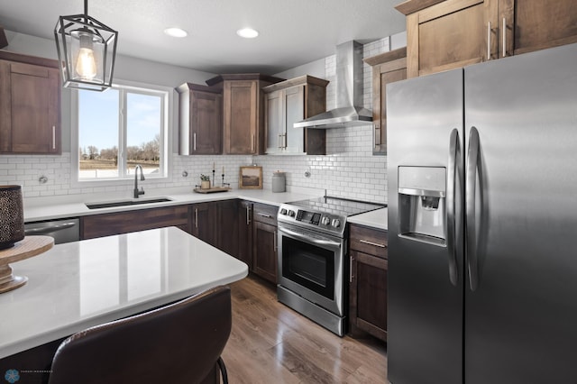 kitchen with wood finished floors, a sink, stainless steel appliances, light countertops, and wall chimney range hood