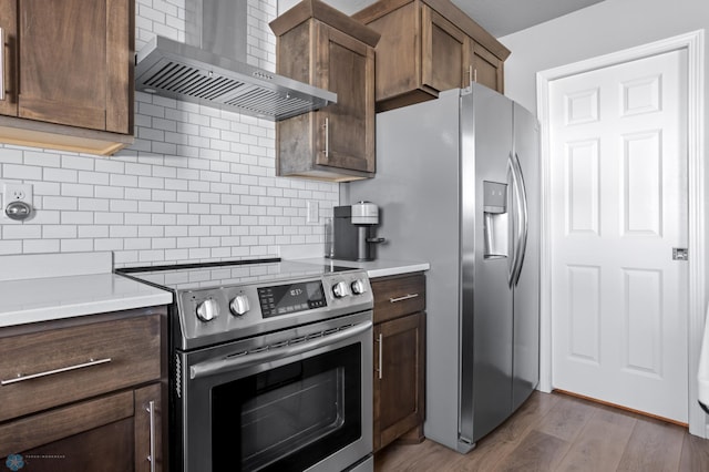 kitchen featuring wall chimney range hood, light countertops, decorative backsplash, wood finished floors, and stainless steel appliances