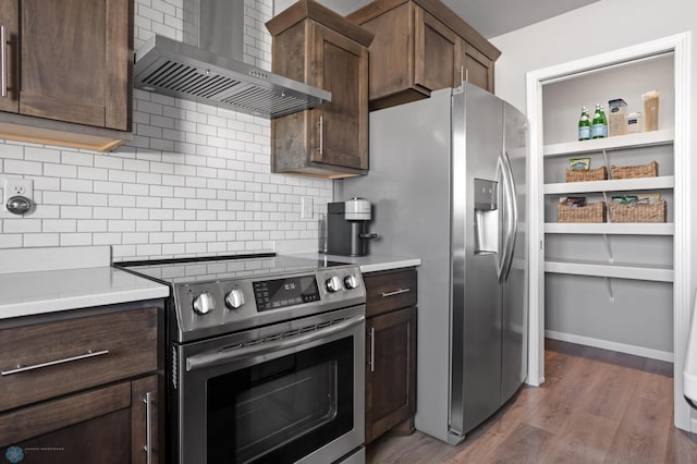 kitchen with tasteful backsplash, wood finished floors, dark brown cabinetry, appliances with stainless steel finishes, and wall chimney range hood