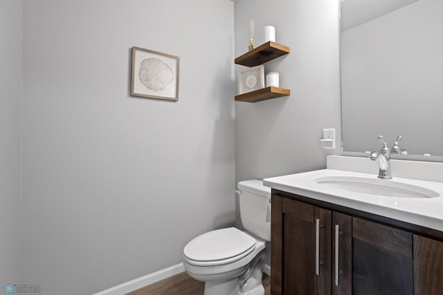 half bath with baseboards, toilet, wood finished floors, and vanity