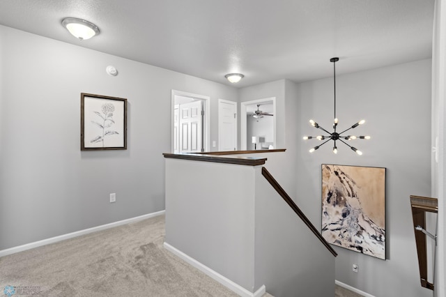 corridor with carpet flooring, an upstairs landing, baseboards, and a chandelier