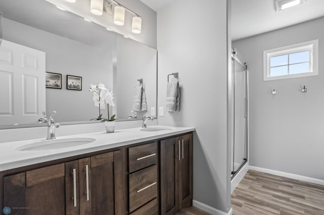 full bath featuring double vanity, baseboards, a stall shower, and a sink