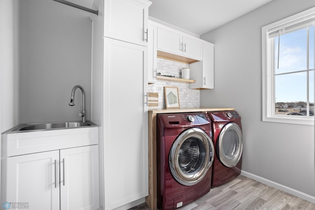 washroom featuring baseboards, cabinet space, a sink, light wood-style floors, and washing machine and dryer