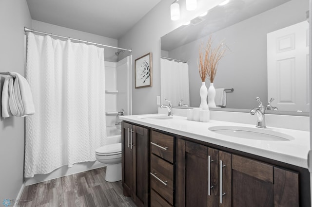 bathroom with double vanity, toilet, wood finished floors, and a sink