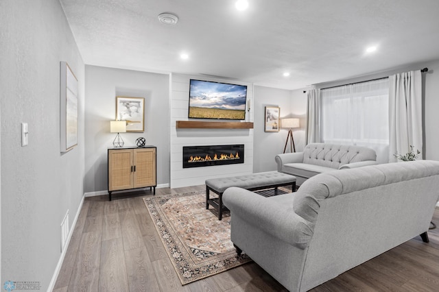 living room featuring visible vents, baseboards, recessed lighting, a fireplace, and wood finished floors