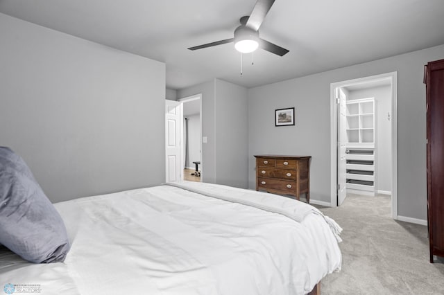 bedroom featuring ceiling fan, a spacious closet, baseboards, and light carpet