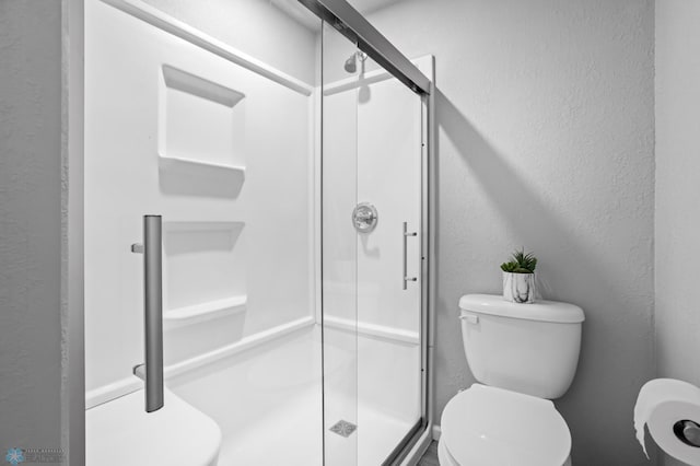 bathroom featuring a shower stall, toilet, and a textured wall