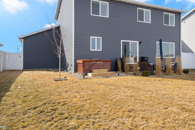 rear view of property featuring a gate, a yard, fence, and a hot tub