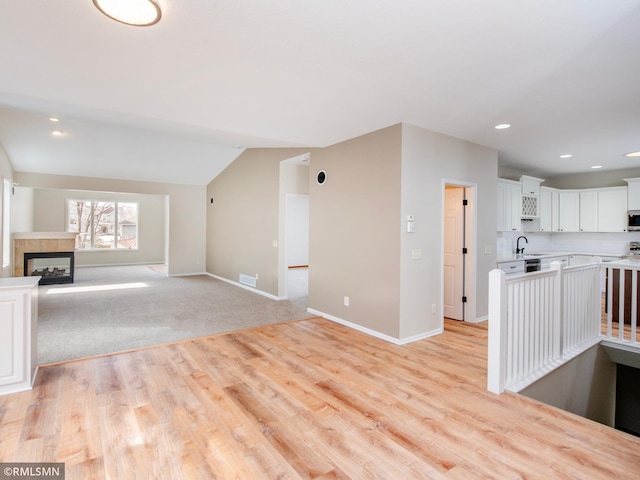 unfurnished living room with baseboards, visible vents, a fireplace, a sink, and vaulted ceiling