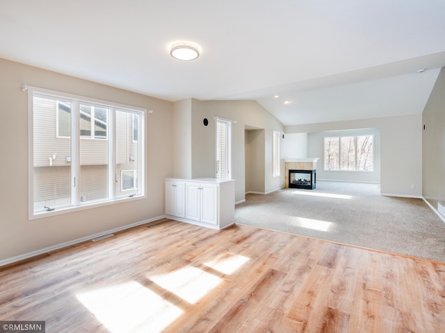 unfurnished living room featuring light wood finished floors, visible vents, baseboards, a tiled fireplace, and lofted ceiling