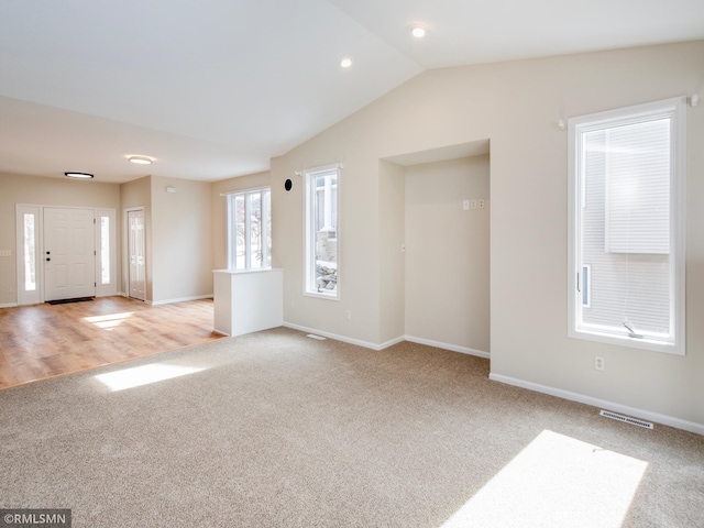 unfurnished living room with baseboards, visible vents, lofted ceiling, and light carpet