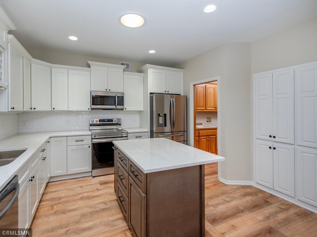 kitchen featuring decorative backsplash, white cabinetry, stainless steel appliances, and light wood-type flooring