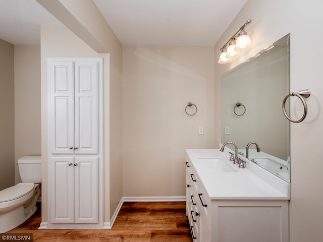 bathroom featuring toilet, vanity, baseboards, and wood finished floors