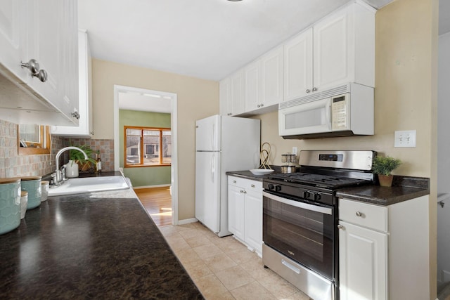 kitchen with white appliances, a sink, decorative backsplash, white cabinetry, and dark countertops