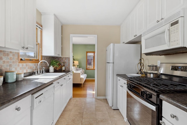 kitchen with dark countertops, tasteful backsplash, white cabinets, white appliances, and a sink