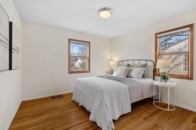 bedroom featuring visible vents, multiple windows, wood finished floors, and baseboards