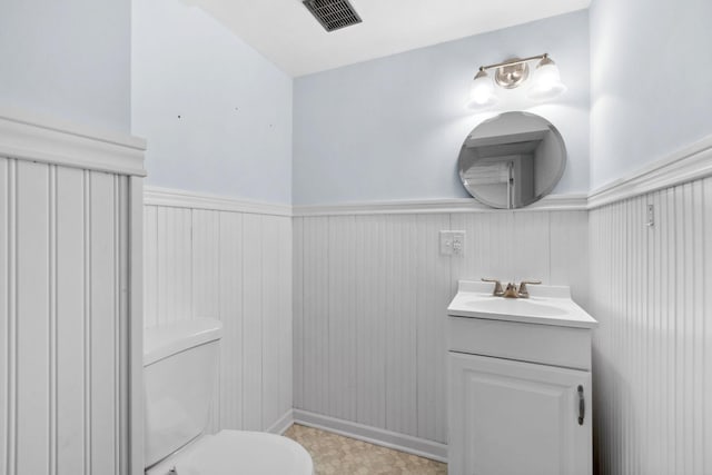 bathroom featuring visible vents, vanity, toilet, and wainscoting