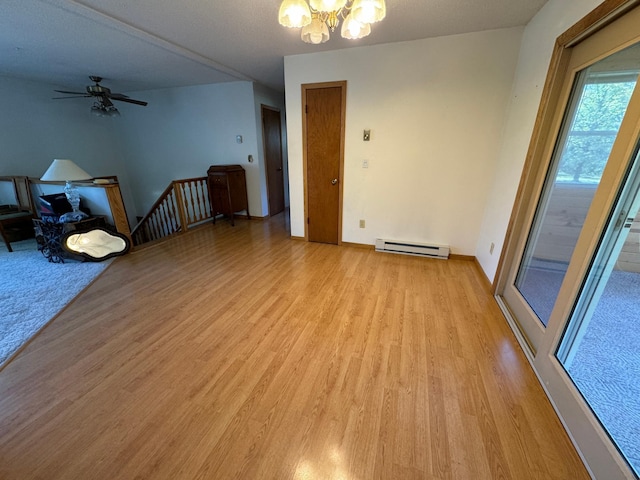 spare room with baseboards, ceiling fan with notable chandelier, baseboard heating, and light wood finished floors