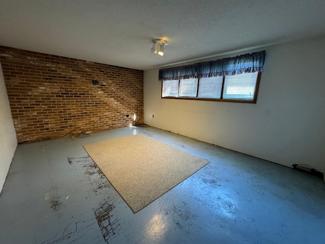 unfurnished room with a textured ceiling, concrete flooring, and brick wall