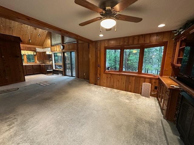 living area featuring vaulted ceiling, wooden walls, a ceiling fan, and carpet floors