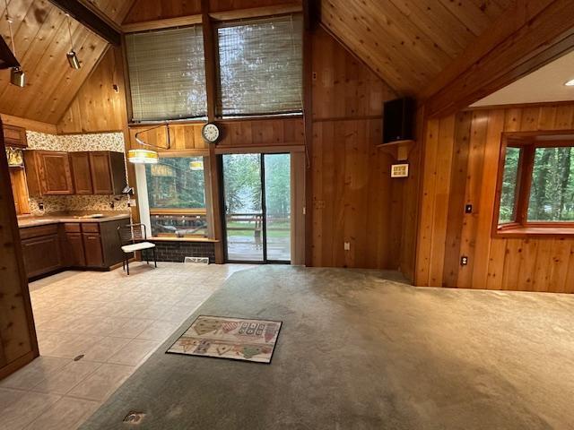 unfurnished living room featuring light tile patterned floors, high vaulted ceiling, wood walls, and wooden ceiling