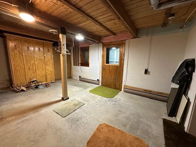 basement featuring a baseboard heating unit, wood ceiling, and concrete block wall