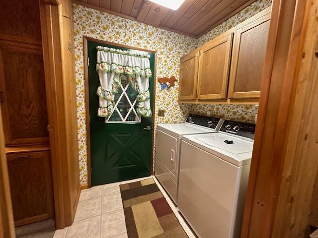 laundry area featuring wallpapered walls, wooden ceiling, cabinet space, and washer and clothes dryer