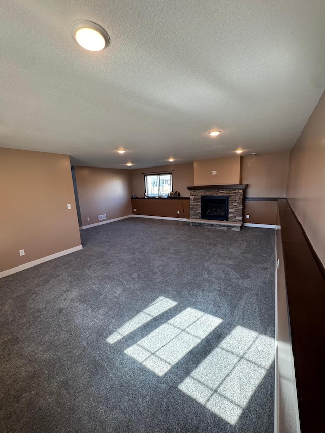 unfurnished living room featuring baseboards, a textured ceiling, a stone fireplace, and carpet flooring