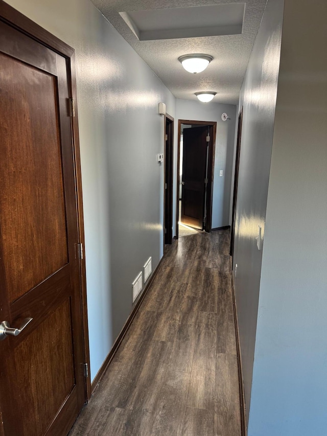 corridor with visible vents, dark wood-type flooring, a textured ceiling, and baseboards