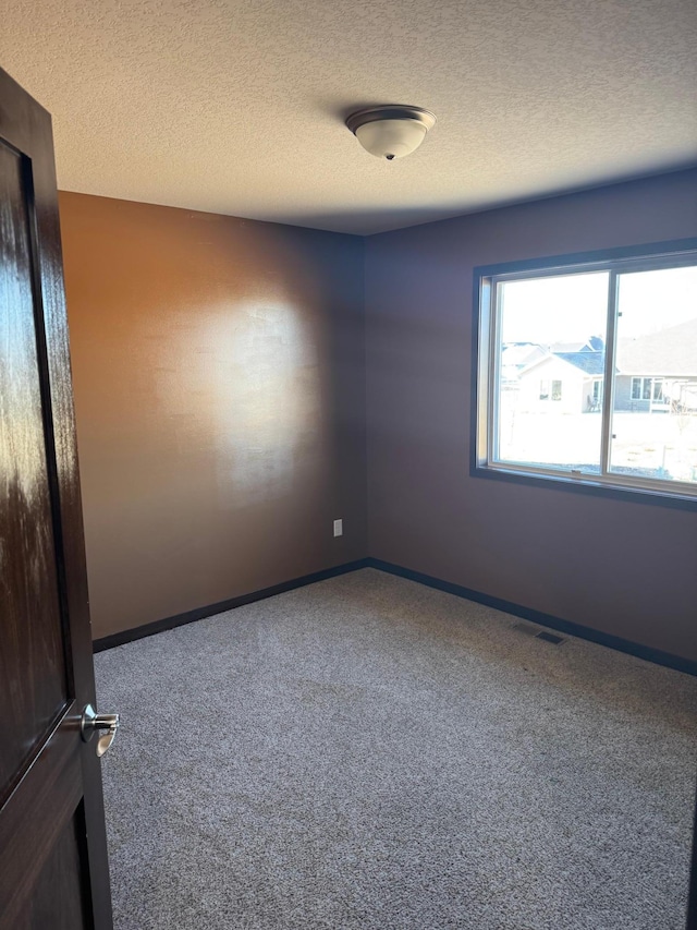 carpeted spare room featuring visible vents, a textured ceiling, and baseboards