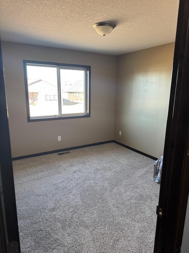 carpeted empty room with visible vents, a textured ceiling, and baseboards