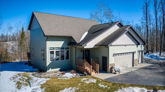 view of front of property with stone siding, driveway, an attached garage, and a shingled roof