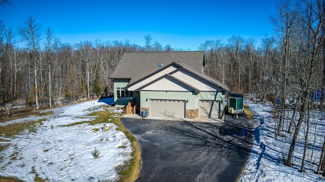 view of front of home with aphalt driveway, a garage, and a wooded view