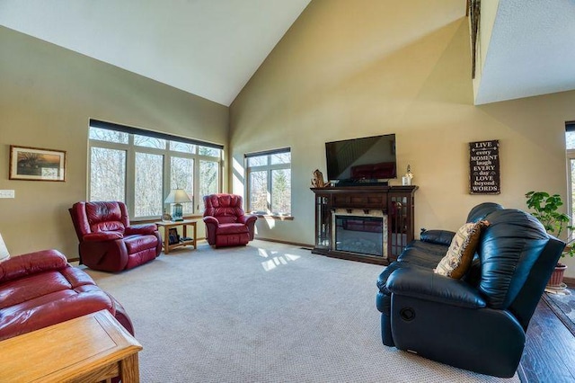 carpeted living area with a glass covered fireplace, baseboards, and high vaulted ceiling