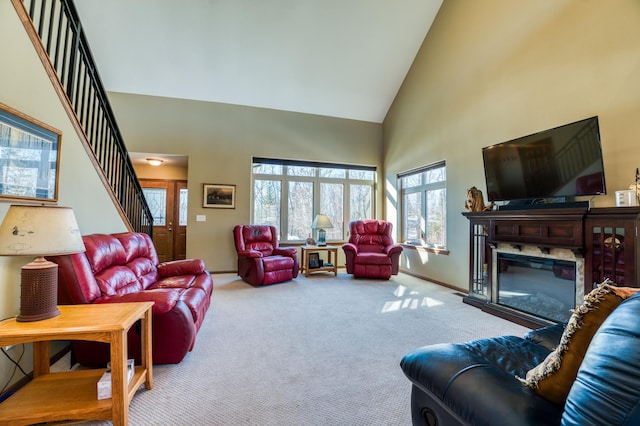 living area with baseboards, carpet, stairs, a glass covered fireplace, and high vaulted ceiling