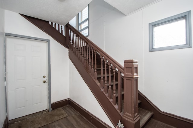 stairway with wood finished floors, baseboards, and a textured ceiling