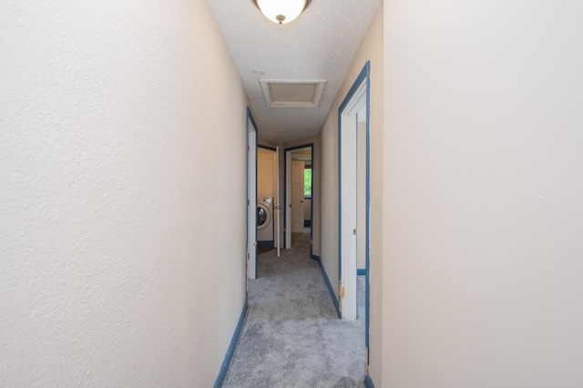 hall featuring washer / clothes dryer, a textured ceiling, carpet flooring, attic access, and a textured wall