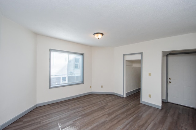 unfurnished bedroom featuring dark wood-style floors, baseboards, a spacious closet, a closet, and a textured ceiling