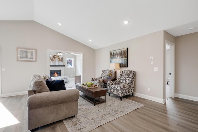 living room featuring wood finished floors, baseboards, recessed lighting, vaulted ceiling, and a glass covered fireplace