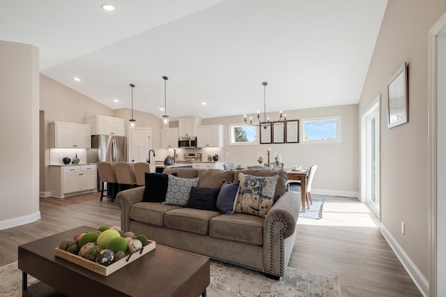 living room featuring light wood finished floors, baseboards, lofted ceiling, recessed lighting, and an inviting chandelier