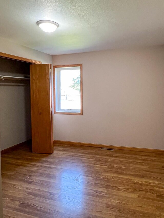 unfurnished bedroom featuring visible vents, baseboards, wood finished floors, a closet, and a textured ceiling