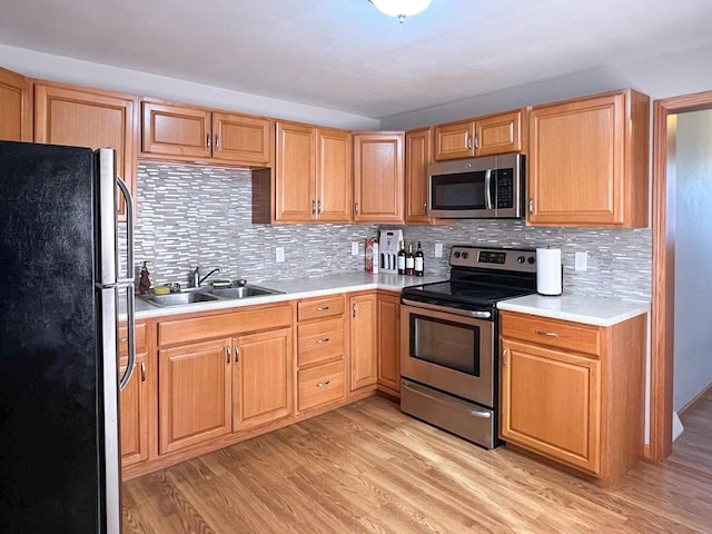 kitchen with light wood-style flooring, a sink, decorative backsplash, light countertops, and appliances with stainless steel finishes