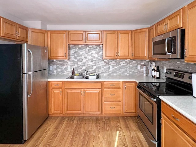 kitchen with a sink, light countertops, light wood-type flooring, and stainless steel appliances